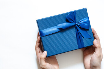 hands hold a gift box tied with a blue ribbon on a white background. Top view, flat lay, giving...