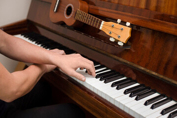 A young guy plays a complex piece of music on the piano, his hands lie on the keys in a cross, the guy loves music very much and often plays both the piano and ukulele