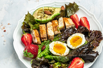 Plate with keto diet food. Keto breakfast Fried egg, avocado, strawberry, grilled chicken fillet, nuts and fresh salad, Ketogenic diet. Healthy food concept, top view