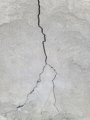 Long vertical uneven crack on the concrete surface. Cracked wall covered with gray cement mortar. Destruction after the earthquake. Copy space. Texture background. Repair, construction of buildings.