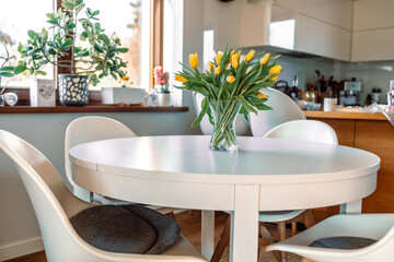 Spring flowers in glass vase on white wooden table in living room. Bouquet of yellow tulips. Contemporary elegant scandi interior. High quality photo