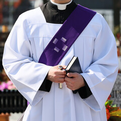 Ksiądz katolicki w komży z fioletowa stułą podczas celebracji pogrzebu. 