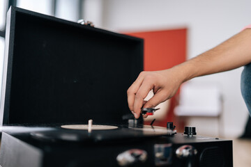 Close-up unrecognizable male hands adjusting head old record player and vinyl discs. Music lover man listening to classical music at home. Hipster guy listening to music on vinyl player.