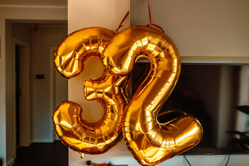 Number 32 thirty two made of gold inflatable balloons on white wall background at home. Golden helium balloons forming 32 thirty two. Birthday concept