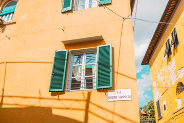 Fototapeta na wymiar Windows on the yellow painted facade of the house. Window with green shutters on a yellow house. Colorful architecture in Pisa, Italy.