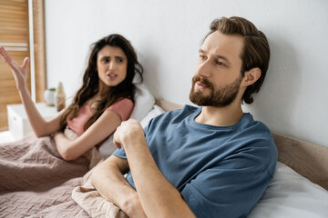 Indifferent man looking away while angry girlfriend quarrelling in bedroom.