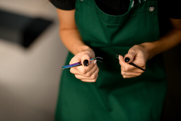 close-up view of the female hands of the master beautician holding steel tweezers.