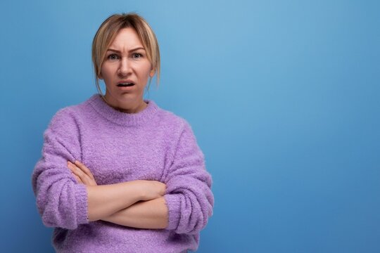 doubting blond woman looking contemptuously at camera on blue background with copy space