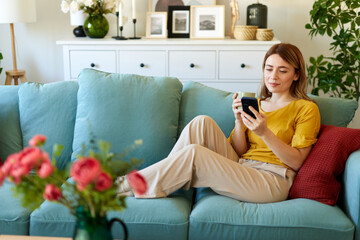Woman using smartphone while drinking coffee at her home in the morning
