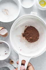 Cocoa powder in a white sieve, sifting cocoa powder into a large bowl