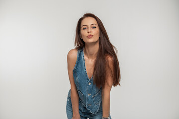 Beautiful young woman model in fashion denim clothes with a denim vest and jeans posing and making a kiss on a white background