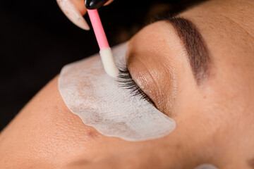 close-up view of closed eye of female and beautician spreads eyelashes with cotton swab