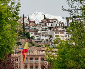 Veleta Peak over Granada houses with flag of Spain in foreground.