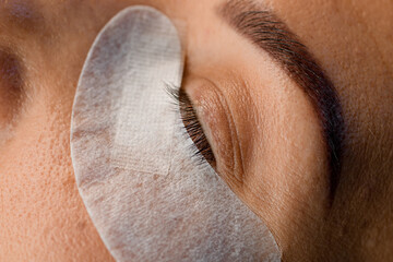 Great close-up view of female face with disposable paper patch under the eye. Eyelash extension