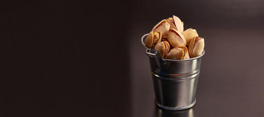 Pistachios in a small metal bucket on a black background.