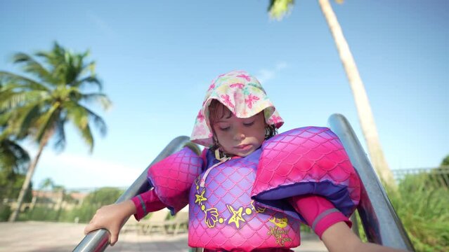 Little girl with floaties standing by stairs outside swimming pool and calling for mom