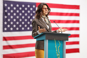 Young woman on a pedestal giving a speech and gesturing with hands with USA flag in the background