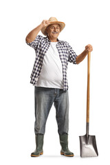 Full length portrait of a happy mature farmer with a shovel greeting with hat - obrazy, fototapety, plakaty