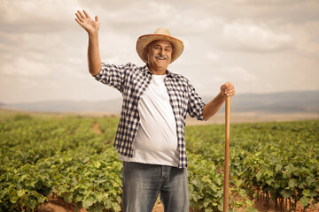 Mature farmer with a shovel greeting from a grapevine field