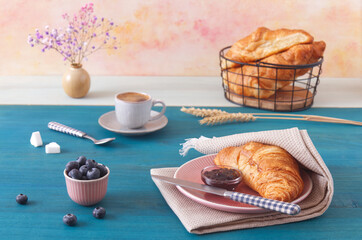Tasty breakfast with croissants, fresh blueberries, jam and cup of coffee. Blue wooden table, low angle of view, no people.