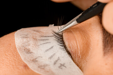 beautiful close-up of beautician gently attaches artificial eyelashes with tweezers. Eyelash extension procedure.