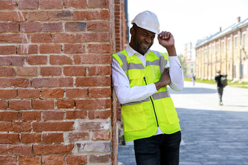 Happy foreman standing touching his helmet in the building wall. Smiled boss after work, looking at...