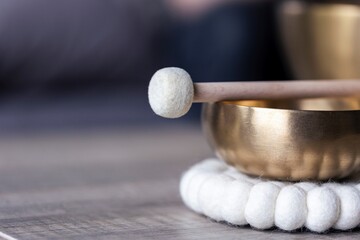 A close portrait of a tibetan singing bowl or himalayan bowl, with a mallet lying on top of it to make a relaxing sound. The object is used for meditation, relaxation and therapy to relieve stress. - obrazy, fototapety, plakaty