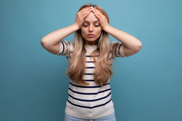 close-up of a sad girl in casual clothes holding her head on a blue isolated background