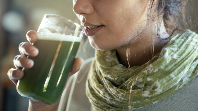 Young woman drinks a glass of green healthy smoothie