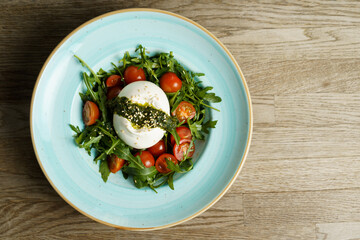 Burrata Caprese Salad with Arugula, Pesto, and Tomato in a plate on a wooden table