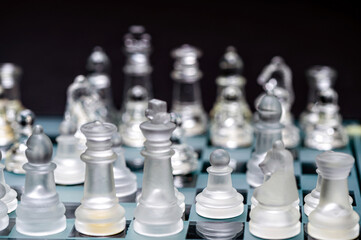 glass, transparent chess pieces on a checkerboard, selective focus, close-up, isolated on black