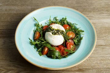 Burrata Caprese Salad with Arugula, Pesto, and Tomato in a plate on a wooden table