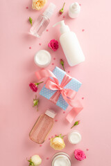 Soft floral beauty concept. Top view flat lay of pump bottle, pipette, cream bottles and tubes with flowers present box on pastel pink background