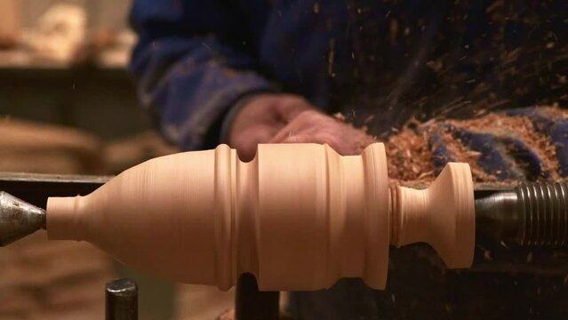 Super slow motion of a wood turner turning a part on his lathe with the wood chips jumping out