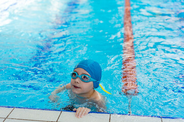 little caucasian boy wearing goggles looking out from swimming pool