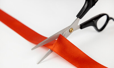 Close-up of scissors cutting a red satin ribbon.