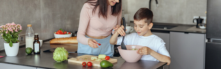 Happy Caucasian mother teaching small son to cook vegetables salat at home.