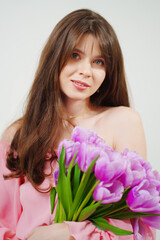 Obraz na płótnie Canvas beautiful young brunette woman with long hair in pink with a bouquet of tulips. 