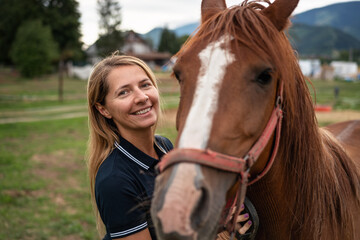 Young woman cleaning brown horse with brush, her head next to animal