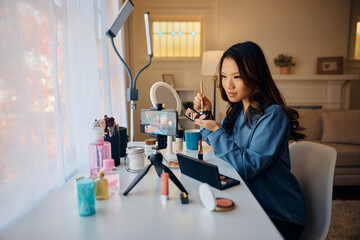 Asian influencer using eyeshadow while recording makeup tutorial for her social media channel.