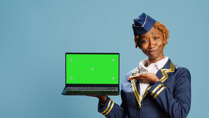 Air hostess holding laptop with green screen display, pointing st blank chroma key template on pc. Aircrew member using computer with isolated copyspace screen, mockup background.