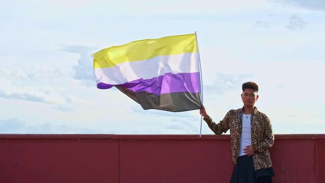 young gender non binary asian person from the front holding a non binary flag blowing in the wind