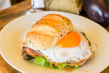 Uruguayan chivito sandwich plate with vegetables and fried egg on homemade French bread in restaurant
