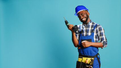 African american man using power drilling tool on wall, drill nails with cordless nail gun on camera. Professional handyman with overalls holding drill gun for holes, construction equipment.