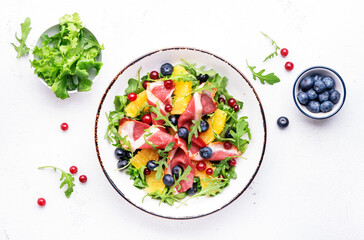 Gourmet salad with smoked duck fillet, fruit and berries, arugula and lettuce, white table background, top view