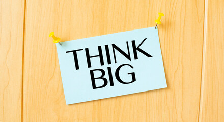 THINK BIG sign written on sticky note pinned on wooden wall