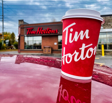 oshawa, canada - 19 October 2022: cup of tim hortons coffee on red car in front of outlet with logo