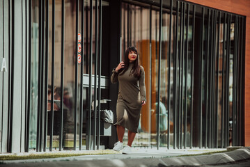 A confident and stylish plus-size woman walking by a modern building in an olive green dress, radiating beauty, empowerment, and self-love.