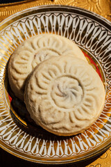 close up of two maamoul (ma'amoul), date-filled butter cookies on ornate patterned gold and white plate