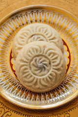 close up of two maamoul (ma'amoul), date-filled butter cookies on ornate patterned gold and white plate